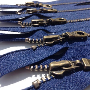 May include: A close-up of several navy blue zippers with antique brass pulls. The zippers are arranged in a fan shape, with the pulls facing the viewer.