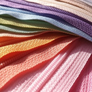 May include: A close-up of a rainbow assortment of zipper tape. The tape is arranged in a fan shape, with the colors transitioning from purple to pink to orange to yellow to green to blue.