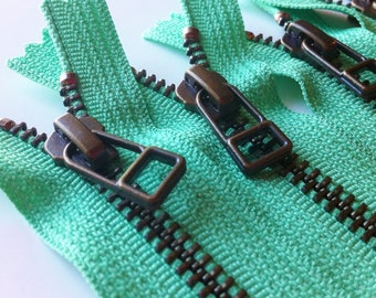 Op de afbeelding: Close-up van drie groene ritsen met zwarte tanden en antieke messing schuifjes.