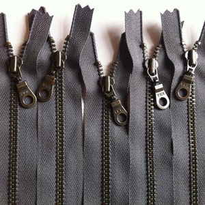 May include: Eight gray metal zippers with silver teeth and antique brass pull tabs. The pull tabs have the text "YKK" on them.