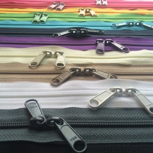 May include: Assortment of colorful zipper pulls in various colors, including red, green, yellow, purple, beige, brown, white, and black. The zipper pulls are all metal and have the brand name "YKK" printed on them.