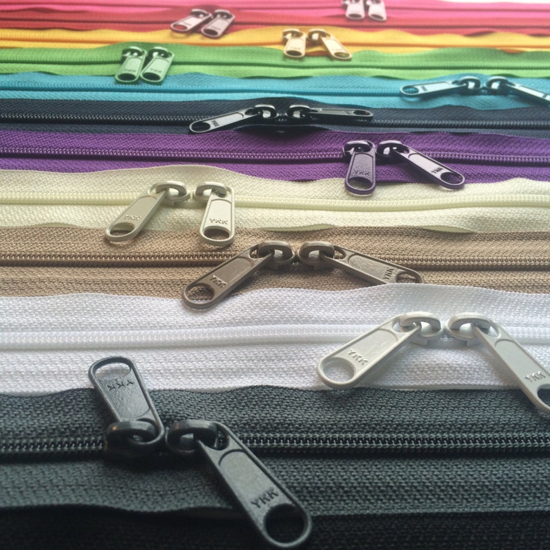 May include: Assortment of colorful zipper pulls in various colors, including red, green, yellow, purple, beige, brown, white, and black. The zipper pulls are all metal and have the brand name "YKK" printed on them.