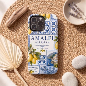 May include: A phone case featuring a design inspired by Amalfi, Italy. The case has a blue and white tile pattern with lemons and the text "AMALFI ITALIA". The design includes images of the coastline and the words "SOLE MARE AMORE".