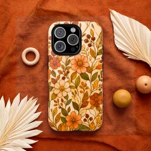 May include: A smartphone case featuring a cream background with a repeating pattern of orange, yellow, and brown flowers, leaves, and berries. The case has a black camera module cutout at the top left corner, showcasing a multi-lens camera system.