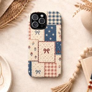 May include: A patterned phone case with a patchwork design. The case features squares of blue, cream, and pink with bow and star motifs. The camera lenses are visible at the top.