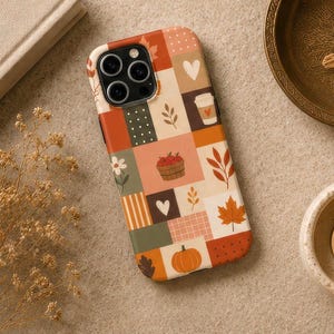 May include: A smartphone case featuring a patchwork grid design with autumn-themed illustrations including a pumpkin, a basket of apples, maple leaves, hearts, a coffee cup, and various patterns in shades of orange, brown, cream, and sage green.