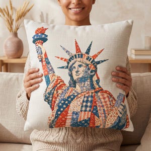 May include: A decorative square pillow featuring a patriotic design of the Statue of Liberty. The image is a collage of red, white, and blue patterns, including stars and stripes. The pillow has a neutral background.