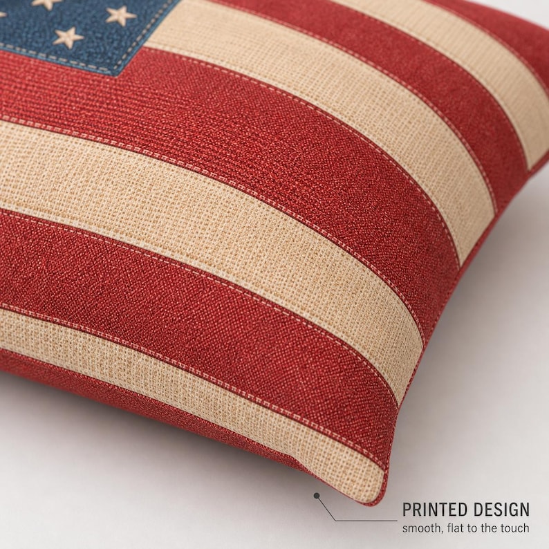 May include: A decorative pillow featuring a printed design of the American flag. The pillow has red and beige stripes, a blue corner with white stars, and the text "PRINTED DESIGN smooth, flat to the touch".
