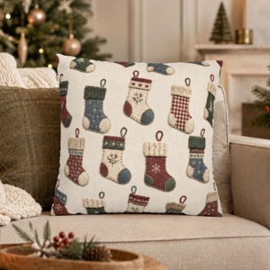 May include: A square throw pillow with an off-white background featuring a repeating pattern of embroidered Christmas stockings in various colors including red, blue, green, and cream, each decorated with unique snowflake and floral motifs.