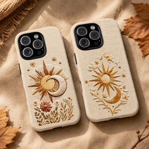 May include: Two beige phone cases featuring embroidered designs. The left case displays a sun and crescent moon with a flower, while the right case shows a sun and moon with star accents. Both cases have a textured fabric-like finish.