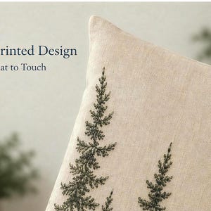 May include: A beige throw cushion cover featuring a dark green printed design of pine tree branches. The text Printed Design Flat to Touch is visible in the upper left corner. The fabric has a visible woven texture and a neutral light beige colour.
