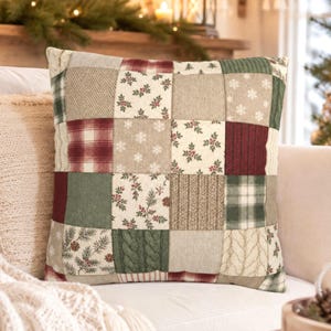 May include: A square throw pillow featuring a patchwork design of various fabric squares in shades of red, green, cream, and beige. The patterns include plaid, herringbone, cable knit textures, holly berries, pine branches, and white snowflakes.