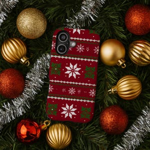 May include: A red phone case with a festive snowflake and geometric pattern, surrounded by Christmas ornaments and evergreen branches. The case features white and green accents, creating a holiday sweater design.