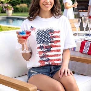 White comfort colors t-shirt with distressed american flag and subtle floral overlay, styled as patriotic summer graphic tee for women.