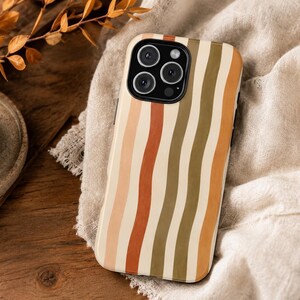 May include: A smartphone case featuring a pattern of vertical, wavy stripes in shades of cream, terracotta, olive green, and mustard yellow. The case has a black camera cutout area with three circular lenses and a flash.