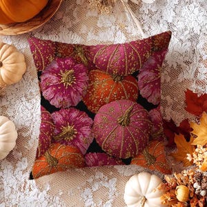 May include: Square decorative pillow featuring a pattern of embroidered pumpkins in shades of pink and orange with gold accents. The pumpkins are set against a black background. The pillow is surrounded by fall-themed decorations.