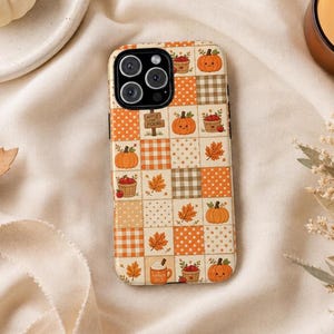 May include: A smartphone case featuring a patchwork design of orange, cream, and brown squares. The pattern includes illustrations of smiling pumpkins, baskets of apples, autumn leaves, and a mug labeled Pumpkin Spice with a sign saying Apple Picking.