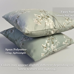 May include: Two decorative throw pillows stacked on top of each other. The pillows have a light green background with a white floral pattern. The top pillow is labeled "Faux Suede" and the bottom pillow is labeled "Spun Polyester".