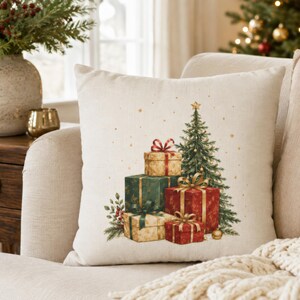 May include: A square off-white throw pillow featuring a printed illustration of a decorated Christmas tree surrounded by a stack of wrapped gift boxes in shades of red, green, and gold, accented with small gold stars and pine greenery.