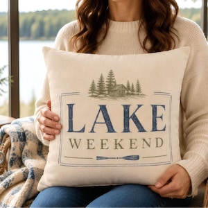 Lake Weekend decorative pillow cover with rustic typography, cabin illustration, and paddle detail on a neutral linen style background for cozy lake house decor.