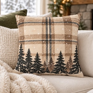 May include: A square throw pillow featuring a beige and tan plaid pattern with a dark forest of pine trees printed along the bottom edge. The design includes small white dots scattered across the plaid, resembling falling snow in a winter forest.