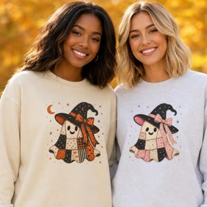 May include: A beige sweatshirt featuring a patchwork ghost wearing a black witch hat with an orange bow, and a light gray sweatshirt featuring a patchwork ghost wearing a black witch hat with a pink bow, both with small star and moon accents.