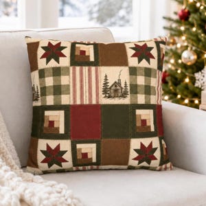 May include: A square throw pillow featuring a patchwork design with alternating blocks of dark red, forest green, and cream. The pattern includes star motifs, log cabin blocks, striped squares, and a central illustration of a cabin in the woods.