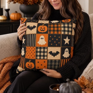 May include: A square throw pillow featuring a patchwork design with alternating blocks in black and orange. The pattern includes illustrations of jack-o'-lanterns, white ghosts, black bats, stars, and various plaid and striped fabric textures.