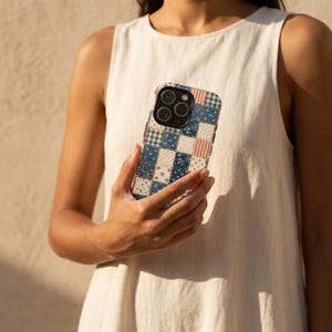 Op de afbeelding: Telefoonhoesje met een patchworkpatroon met een mix van blauwe, rode en cr&egrave;mekleurige vierkanten. Het ontwerp bevat bloemen-, ruit- en streepmotieven. De hoes heeft een camera-uitsparing en een zwarte rand.