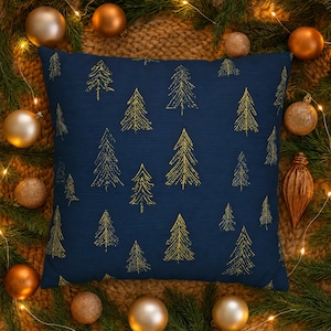 May include: A square throw pillow with a deep navy blue fabric base featuring a repeating pattern of gold-colored line-drawn pine trees. The trees are depicted in a simple, stylized manner with thin, vertical strokes forming the branches.
