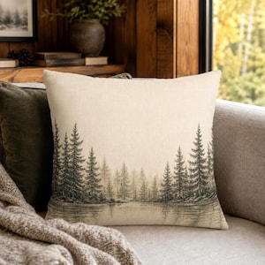 May include: A square throw pillow with a light beige linen-like texture featuring a dark gray printed illustration of a dense pine forest bordering a calm body of water. The design spans the lower portion of the pillow cover with detailed trees.