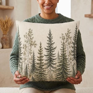 May include: A square throw pillow featuring a detailed forest print with various evergreen and deciduous trees in shades of dark green and muted brown against a light cream-colored background. The design covers the entire front surface.
