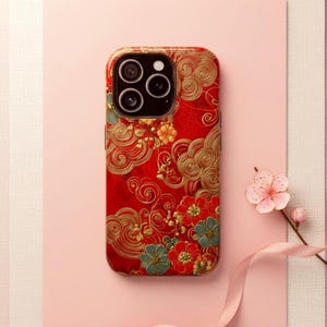 May include: A smartphone case featuring a vibrant red background adorned with intricate gold swirling cloud patterns and detailed floral motifs in shades of red, gold, and teal. The case includes a cutout for a triple-lens camera system.