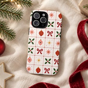 May include: A white smartphone case featuring a repeating grid pattern of red and pink Christmas ornaments, green holly leaves, red bows, and gold starbursts. The case has a black camera cutout area with three circular lenses.