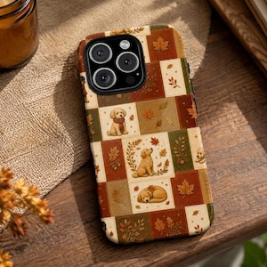 May include: A smartphone case featuring a patchwork design of autumn-themed squares. The pattern includes illustrations of golden retriever puppies, falling maple leaves, acorns, and foliage in shades of brown, orange, cream, and muted green.