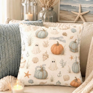 May include: A square throw pillow featuring a cream-colored fabric printed with a repeating pattern of light blue and orange pumpkins, white ghosts, seashells, starfish, anchors, and lanterns, creating a coastal autumn theme.