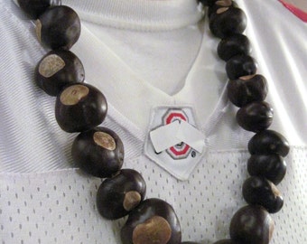 May include: A necklace made of brown buckeye nuts. The necklace is worn by a person wearing a white jersey with a red and white logo.