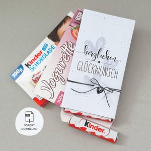 Könnte beinhalten: Eine Auswahl an Kinder Schokoriegeln und eine Geschenkbox mit dem Schriftzug "Herzlichen Glückwunsch" in schwarzer Schrift. Die Geschenkbox ist mit einer schwarzen Schnur und einem kleinen Herz gebunden. Das Bild enthält auch ein "SOFORT DOWNLOAD" PDF-Symbol.