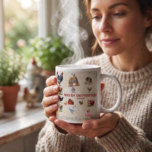 May include: A white ceramic mug featuring a colorful pattern of various chickens, a red barn, and a wagon. The text "Here for the Fresh Eggs and Gossip" is printed in the center. Steam rises from the top of the mug, which has a curved handle.