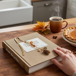 May include: A still-life image featuring a book titled "Autumn Harvest Pies" with a decorative bookmark. A cup of coffee, a slice of pie, and fall foliage are also present, creating a cozy autumn theme.