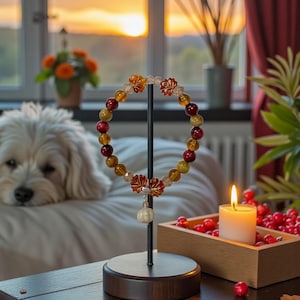 May include: A beaded bracelet with red, yellow, and clear beads is displayed on a black stand. The bracelet has decorative floral accents. A lit candle and a wooden box with red berries are on a dark wooden table.