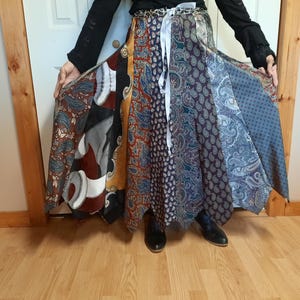 May include: A long, multi-colored skirt made from different patterned fabrics. The skirt is tied at the waist with a white ribbon and has a flowing, layered design.