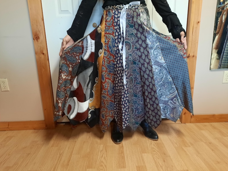 May include: A long, multi-colored skirt made from different patterned fabrics. The skirt is tied at the waist with a white ribbon and has a flowing, layered design.