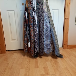 May include: A long, flowing skirt made from repurposed neckties. The skirt is a patchwork of different patterns and colors, including paisley, stripes, and solids. The skirt is tied at the waist with a white ribbon.