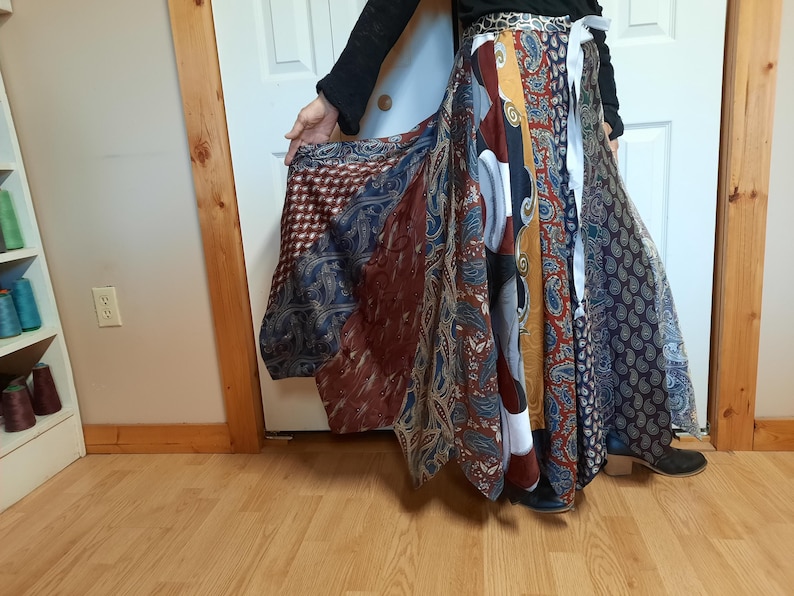 May include: A long, flowing skirt made from a variety of colorful fabrics. The skirt is a patchwork of different patterns and colors, including blue, red, yellow, and white. The skirt is gathered at the waist and falls to the ankles.