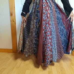 May include: A long, flowing skirt made from repurposed neckties. The skirt is a patchwork of different colored ties, with a predominantly blue and red color scheme. The skirt is gathered at the waist and falls to the floor.