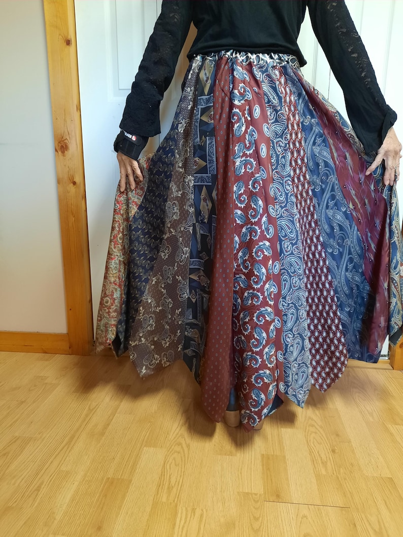 May include: A long, flowing skirt made from repurposed neckties. The skirt is a patchwork of different colored ties, with a predominantly blue and red color scheme. The skirt is gathered at the waist and falls to the floor.