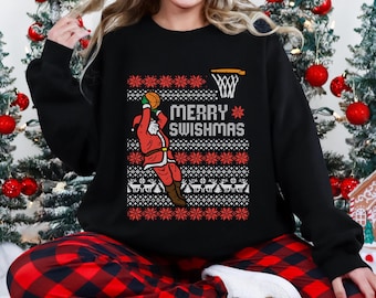 May include: Black sweatshirt with a festive "Merry Swishmas" design. The graphic features Santa Claus playing basketball, with a basketball hoop and snowflakes. The design is in red and white, with a pattern of snowflakes and reindeer.