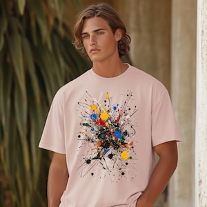 May include: A pink t-shirt with a colorful abstract paint splatter design. The design features black, red, yellow, blue, and green paint splatters.