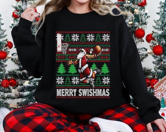 May include: Black sweatshirt with a festive design featuring Santa Claus playing basketball. The graphic includes a basketball hoop, snowflakes, and Christmas trees. The text "MERRY SWISHMAS" is displayed below the image.
